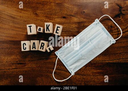 'Take care' Text aus Holz mit medizinischem Maskenwürfel auf Holzhintergrund. Stockfoto