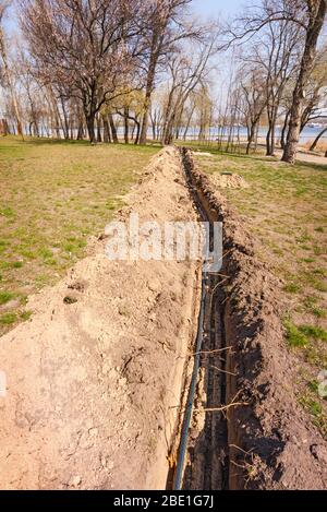 Installation von Rohren für eine Bewässerungssystem im Boden unter den Bäumen in der Nähe des Flusses. Bewässerungssystem im Natalka-Park in Kiew, Ukraine Stockfoto