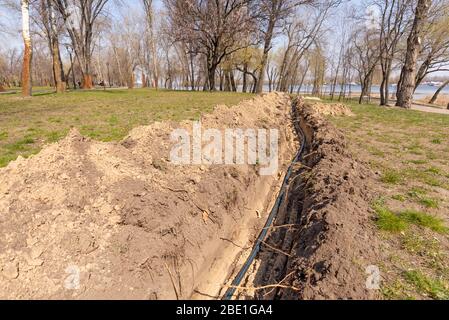 Installation von Rohren für eine Bewässerungssystem im Boden unter den Bäumen in der Nähe des Flusses. Bewässerungssystem im Natalka-Park in Kiew, Ukraine Stockfoto