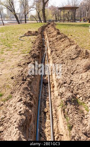 Installation von Rohren für eine Bewässerungssystem im Boden unter den Bäumen in der Nähe des Flusses. Bewässerungssystem im Natalka-Park in Kiew, Ukraine Stockfoto