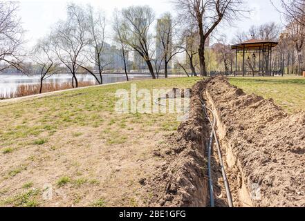 Installation von Rohren für eine Bewässerungssystem im Boden unter den Bäumen in der Nähe des Flusses. Bewässerungssystem im Natalka-Park in Kiew, Ukraine Stockfoto