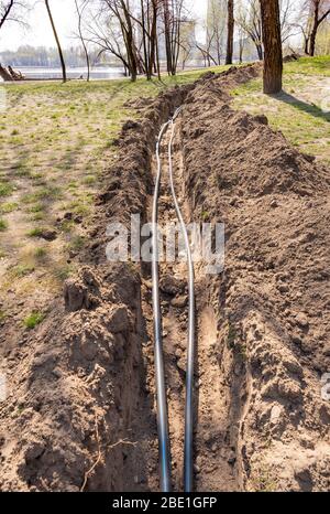 Installation von Rohren für eine Bewässerungssystem im Boden unter den Bäumen in der Nähe des Flusses. Bewässerungssystem im Natalka-Park in Kiew, Ukraine Stockfoto