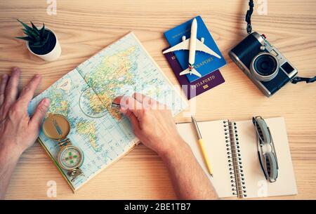 Männliche Hand hält eine Lupe für die Planung Reise mit Weltkarte auf dem Tisch. Reisekonzept. Sonnenbrille, Pässe, Notizbuch, Kompass, ca. Stockfoto