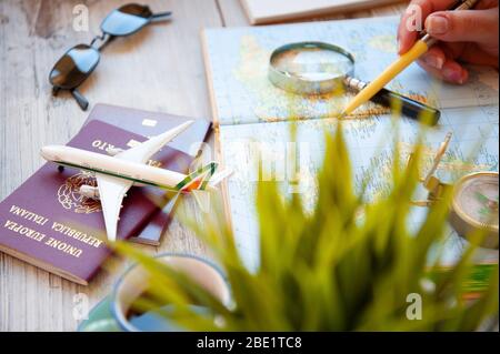 Weibliche Hand hält einen Stift für die Planung Reise mit Weltkarte auf dem Tisch. Reisekonzept. Sonnenbrille, Pässe, Kompass, Spielzeugflugzeug. Das Konzept von Pre Stockfoto