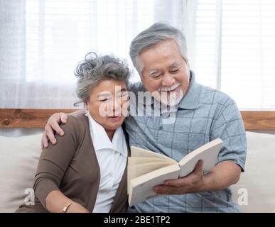 Älteres älteres asiatisches Paar sitzt zu Hause zusammen auf dem Sofa und liest Buch.Mutter Und Großvater verbringen Zeit zusammen im Haus. Stockfoto