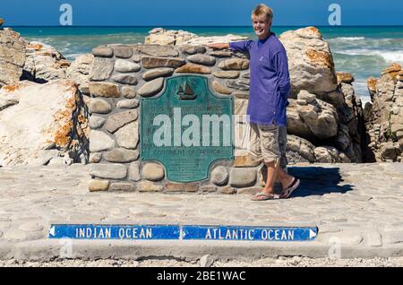 Frau posiert für Foto auf Steindenkmal an der südlichsten Spitze Afrikas, wo Atlantik und Pazifischer Ozean Kap Agulhas Point Südafrika Stockfoto