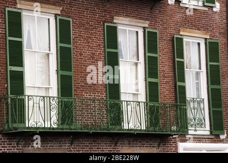 Die verglaste Tür führt zu einem schmiedeeisernen Balkon und ist mit grünen Fensterläden umrahmt. Stockfoto