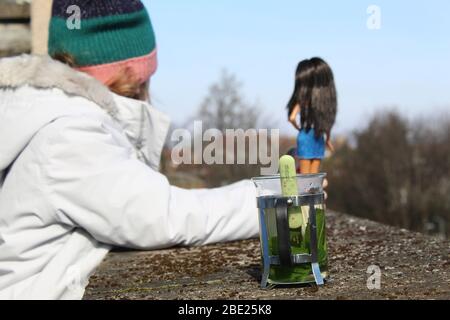 Kind auf dem Balkon mit einer Puppe und Blick in den Horizont mit einer Minze Infusion Stockfoto