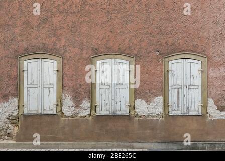 Symmetrische Fassade des verlassenen, baufälligen Hauses mit 3 Fenstern mit Fensterläden Stockfoto