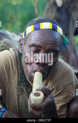 Hadza Mann rauchen von einem traditionellen tonpfeifen fotografiert in der Nähe von Lake Eyasi, Tansania, Afrika Stockfoto