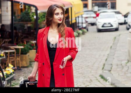 Reisende Geschäftsfrau mit rotem Umhang läuft die Straße hinunter. Stockfoto