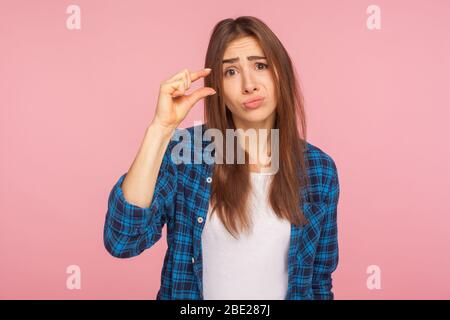 Bitte noch etwas mehr. Porträt von niedlichen Mädchen in karierten Hemd zeigt kleine Größe oder wenig Geste mit Fingern, suchen mit flehenden Grimace. ind Stockfoto