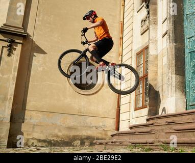 Professionelle Studie Biker führt Stunt fliegen über Betonpflaster, niedrigen Winkel Schuss, architektonisches Gebäude auf Hintergrund Stockfoto