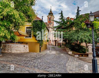 Das historische Gebäude des griechischen Tempels in Vac, Hungary.IT wurde im 18. Jahrhundert gebaut, ist heute eine Ausstellungshalle. Gewundene enge Kopfsteinpflaster Straße Stockfoto