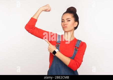 Siehe, ich bin unabhängig und stark! Porträt von zuversichtlich energisch stilvolle Mädchen in Denim Overalls Heben Hand zeigen auf Bizeps, zum Ausdruck bringen, f Stockfoto