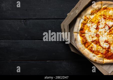 Pizza margherita in offener Lieferbox, dunkle Kulisse mit Textraum. Liefernahrung, Essen zum Mitnehmen Konzept: Stapel von Pizzakartons auf schwarzem Holz zurück Stockfoto