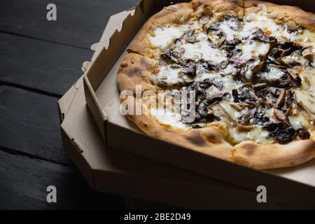 Pizza funghi in einer offenen Lieferbox. Liefernahrung, Essen zum Mitnehmen Konzept: Haufen von Pilzpizzen in Kisten auf schwarzem Holz Hintergrund Stockfoto