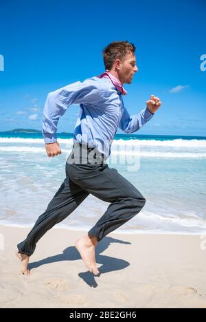 Barfuß-Geschäftsmann, der an einem leeren tropischen Strand entlang läuft Stockfoto