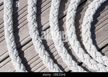 Dickes weißes nautisches Seil, das im Freien auf einem verwitterten Holzdock eine lose abstrakte Spirale bildet Stockfoto