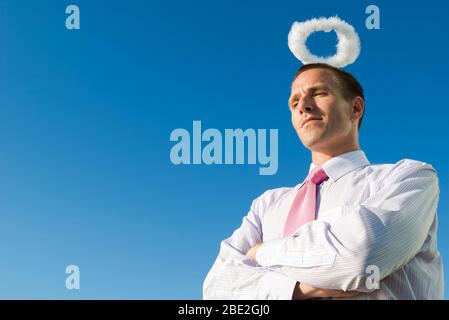 Engelhafte Geschäftsmann mit gefalteten Armen mit einem Heiligenschein über seinem Kopf in den blauen Himmel schweben Stockfoto