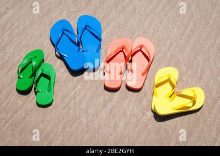 Eine Gruppe von Flip-Flops in hellen Sommerfarben, die am glatten Sandstrand sitzen Stockfoto