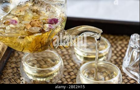 Kräutertee der trocknenden Blumen gießt in Tasse, Nahaufnahme. Eine Teekanne und Tasse mit Blumen Tee auf dem Tisch. Stockfoto