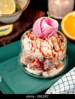 Ein Glas Obstsalat mit Sahne, garniert mit Sirup und Erdbeereis Stockfoto