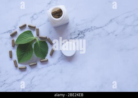 Kräutermedizin in Kapseln mit natürlichem grünen Blatt auf weißem Marmor Stockfoto