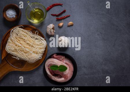 Frisches Fleisch, Rind oder Schweinefleisch auf Holzblock mit Zutaten zum Kochen auf dunklem Zementgrund Stockfoto