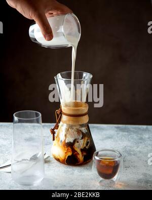 Mann gießt Milch auf Kaffee in einzigartig geformten Glas Stockfoto