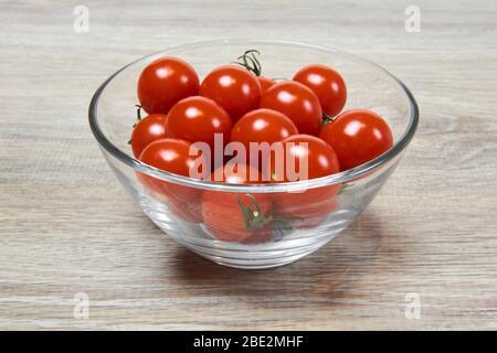 Kleine rote Kirschtomaten in einer Glasschüssel auf einer hölzernen Tischfläche Stockfoto