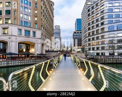 India Place und Cabot Square vereint durch eine Fußgängerbrücke, die in der Abenddämmerung nahe Canary Wharf in London beleuchtet wird. Stockfoto