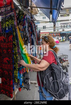 Bangkok, Thailand - 27. Februar 2020: Eine Touristenin, die durch bunte Kleidungsstücke auf einer Bangkok Straße stöbert. Stockfoto