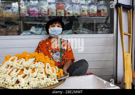 Bangkok, Thailand - 27. Februar 2020: Ein behinderter Blumenhändler, der eine Schutzmaske trägt, auf einer Bangkok Straße. Stockfoto