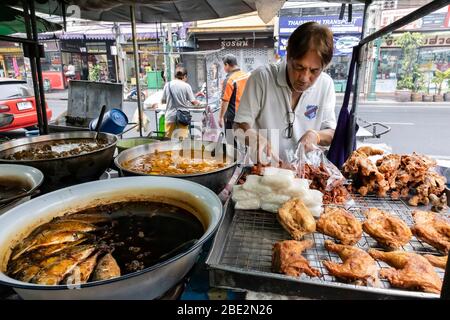 Bangkok, Thailand - 27. Februar 2020: Ein traditioneller Straßenlebensmittelhändler, der Fisch und Huhn auf einer Bangkok Straße verkauft. Stockfoto