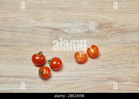 Drei ganze und eine Hälfte in Kirschtomaten auf dem Rand einer hölzernen Tischfläche geschnitten Stockfoto
