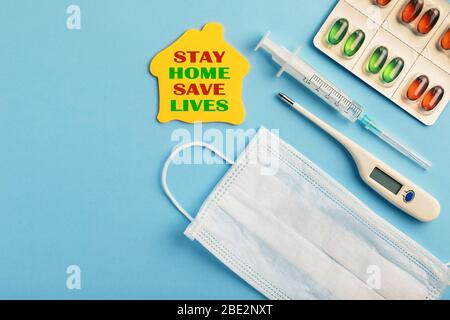 Coronavirus und Stay Home Konzept. Medizinische Gesichtsmaske, Thermometer, Medikapillen und Spritze auf blauem Hintergrund. Flaches Lay, Stockfoto