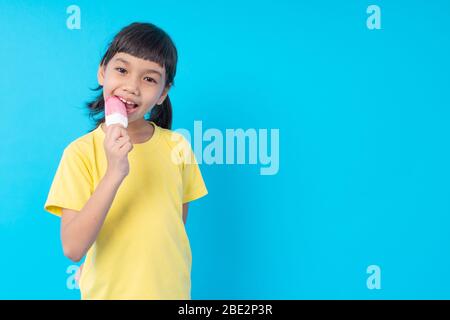 Junge asiatische Mädchen Kind essen Eis und Posting lustig auf blauem Hintergrund im Studio Stockfoto