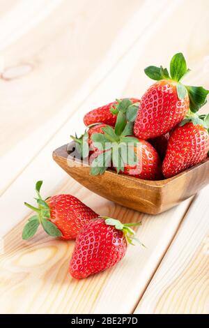 Frische Erdbeeren in Holzschale auf braunem Vintage-Tisch. Rote saftige Erdbeere auf Holzhintergrund. Nahaufnahme. Stockfoto