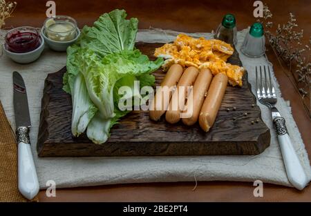 Kontinentales Frühstück mit Rührei, Bratwürsten, Gemüse und Scones auf Holzhintergrund, selektiver Schwerpunkt. Stockfoto