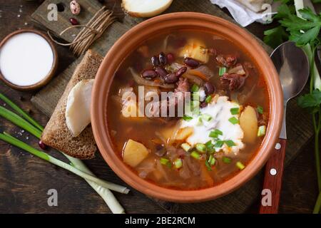 Das Konzept der gesunden Ernährung und Ernährung. Russische oder ukrainische Küche. Suppe mit Fleisch und Bohnen oder Borsch mit saurer Sahne auf einem rustikalen Holztisch serviert Stockfoto