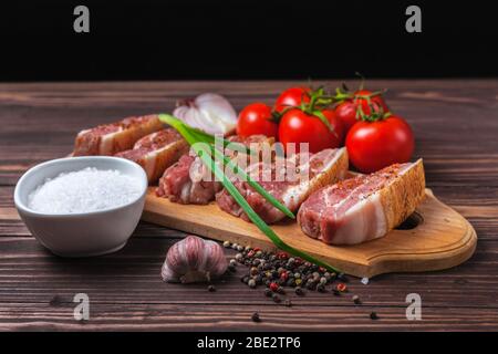 Rohe Scheiben Schweinespeck auf einem Schneidebrett, auf einer ländlichen Holzplatte. Schweinebauch mit Gemüse. Stockfoto
