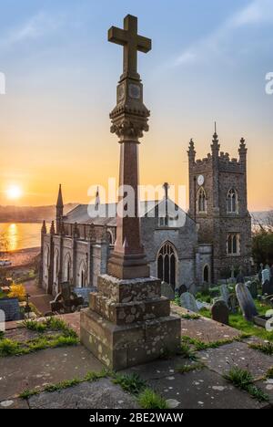 Der ruhige Kirchhof von St. Mary's ist voller Frühlingsblumen, wenn die Sonne über der Flussmündung des Flusses Torridge im Küstendorf Appledore in aufgeht Stockfoto