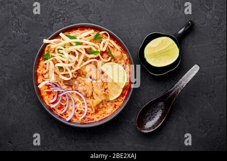 Khao Soi Gai oder Thai Coconut Curry Noodle Suppe in schwarzer Schüssel auf dunklem Schiefergrund. Khao Soy ist Thailand Küche Gericht mit Nudeln, Hühnerfleisch, r Stockfoto