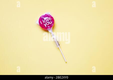 Ein süßes gewickeltes 'I Love You' rotes Lollypop vor einem pastellgelben Hintergrund Stockfoto