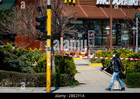 Frau mit Gesichtsschutzmaske geht vorbei an einem geschlossenen für normale Geschäfte McDonald's Fast Food Restaurant, das nur Essen zum Mitnehmen erlaubt aufgrund der Ausbreitung der Coronavirus-Pandemie von Covid-19 in Sofia, Bulgarien seit 2020 Stockfoto