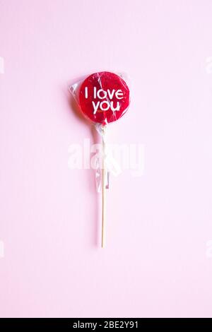 Ein süßes gewickeltes 'I Love You' rotes Lollypop vor pastellgelbem Hintergrund, flaches Lay, Draufsicht, minimalistisch Stockfoto