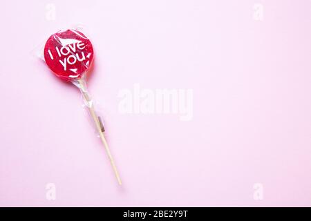 Ein süßes gewickeltes 'I Love You' rotes Lollypop vor pastellgelbem Hintergrund, flaches Lay, Draufsicht, minimalistisch Stockfoto