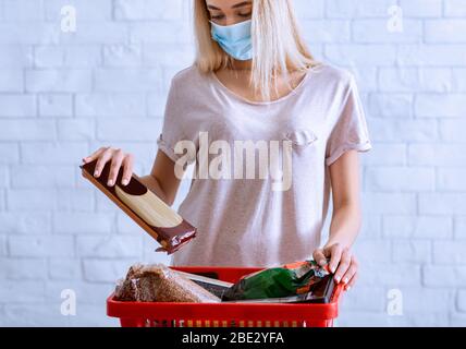 Eine Frau in Maske kauft Lebensmittel und legt den Korb an Stockfoto