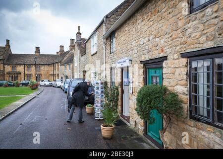 Eine Touristeninspektion führt eine Sammlung von Postkarten vor einem Geschäft in der Nähe der Sherborne Abbey durch. Stockfoto